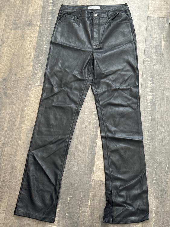 Black synthetic pants with front pockets and a button, on a light wooden floor.