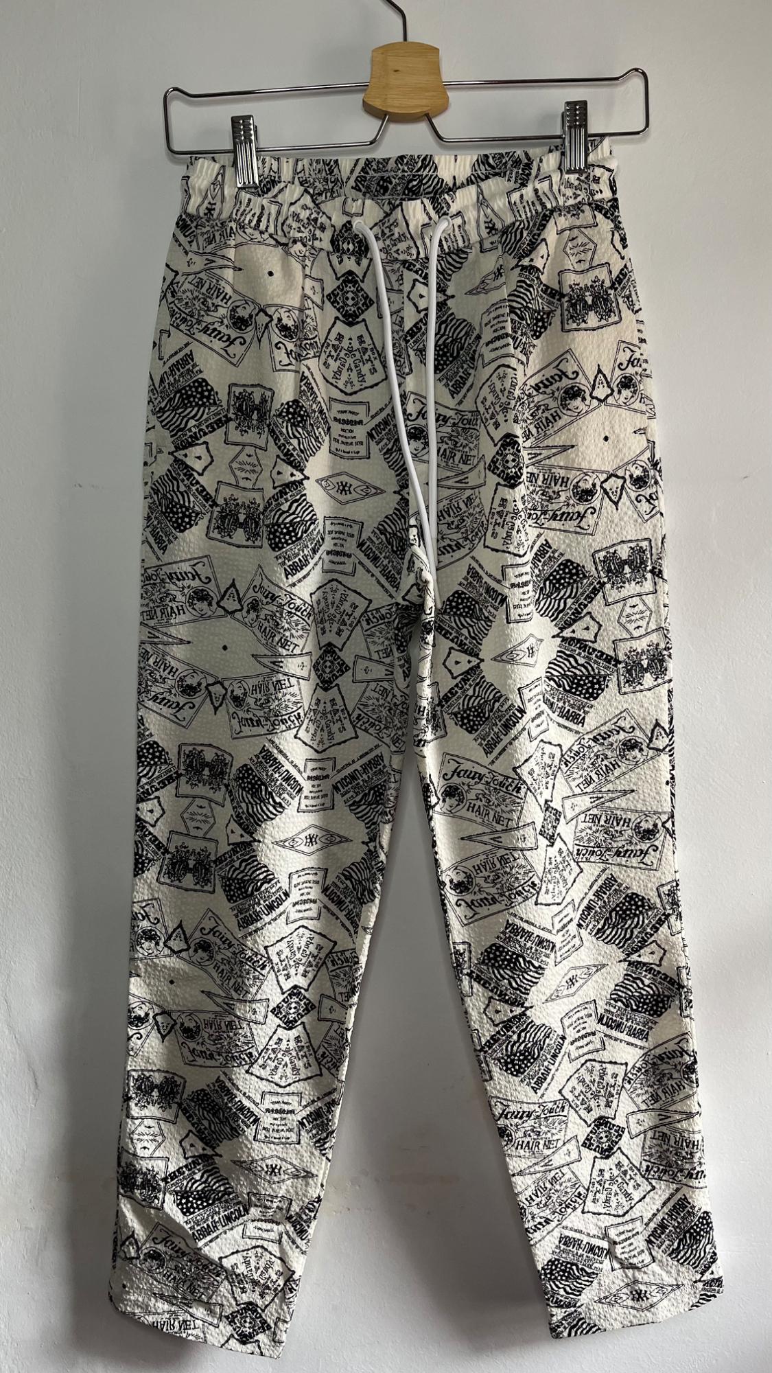 Trousers hanging on a hanger, with a black and white graphic print, white drawstring at the waist, white background.