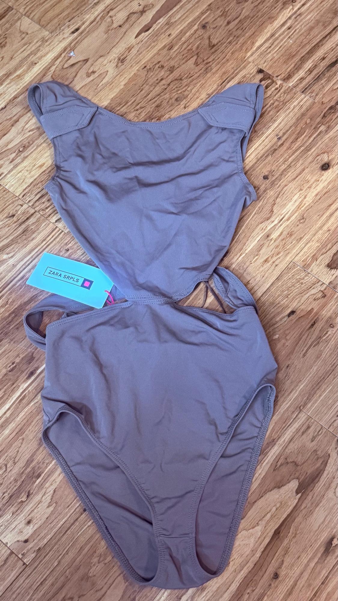 Mauve swimsuit with cutouts at the waist on a wooden floor. It has a blue tag with the text ZARA SRPLS.