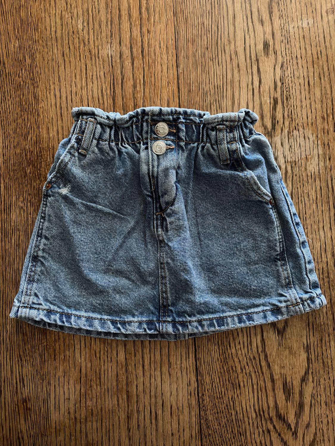 Blue denim skirt with an elasticated waist and two front buttons, on a brown wooden background.