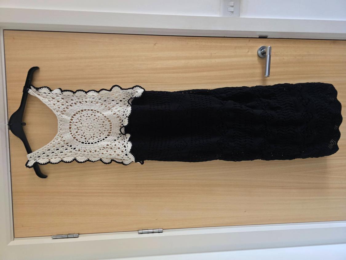 Crochet dress hanging on a wooden door. White top with a circular design and a black bottom.