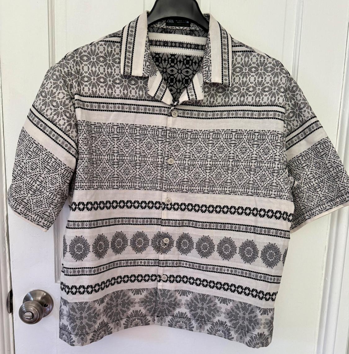Short-sleeved shirt with a black and white geometric print, hanging on a hanger in front of a white door.