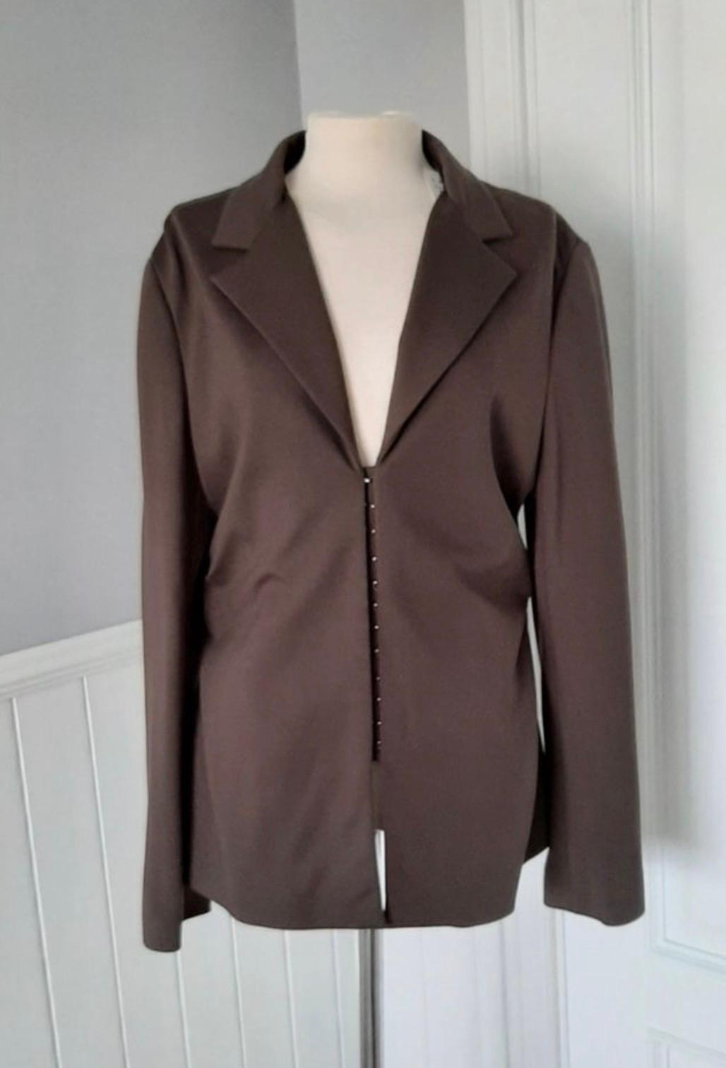 Brown, wide-lapel jacket on a mannequin, light grey and white background, minimalist and elegant setting.