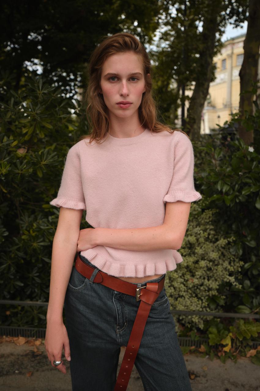 Set aus kurzärmeligem Rundhalspullover in Pastellrosa mit dunkelblauer Jeans und braunem Gürtel.