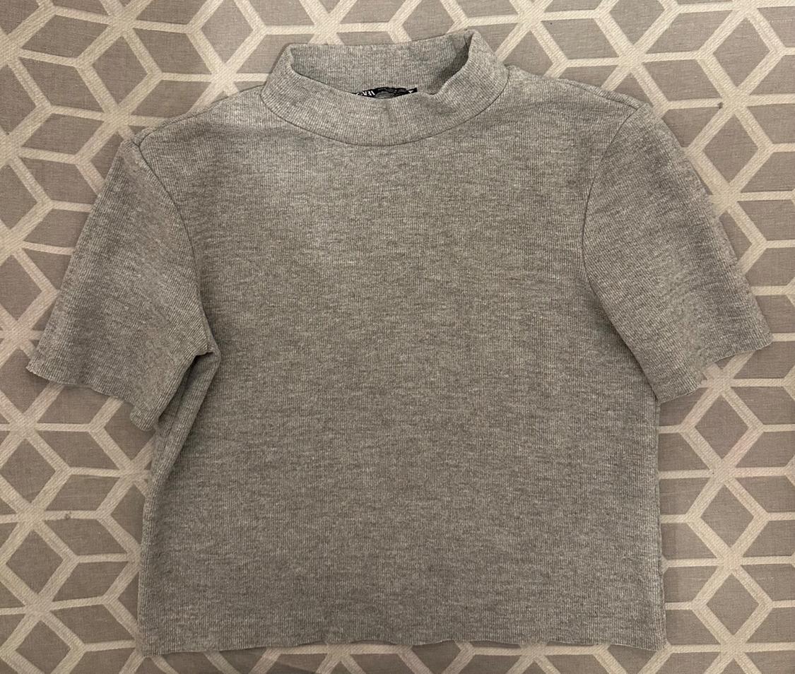 Grey short-sleeved, high-necked t-shirt on a beige and grey geometric background.
