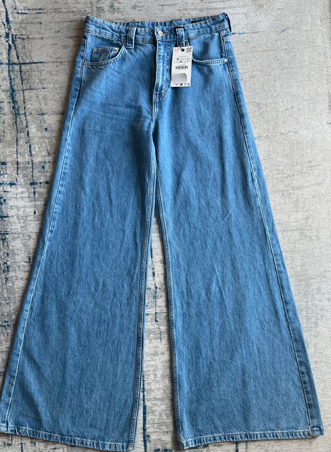 Wide blue denim jeans with a hang tag, on a grey and blue toned rug.