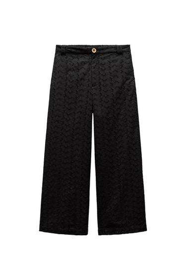 Black, straight-leg trousers with floral embroidery pattern and brown button at the waist, on a white background.