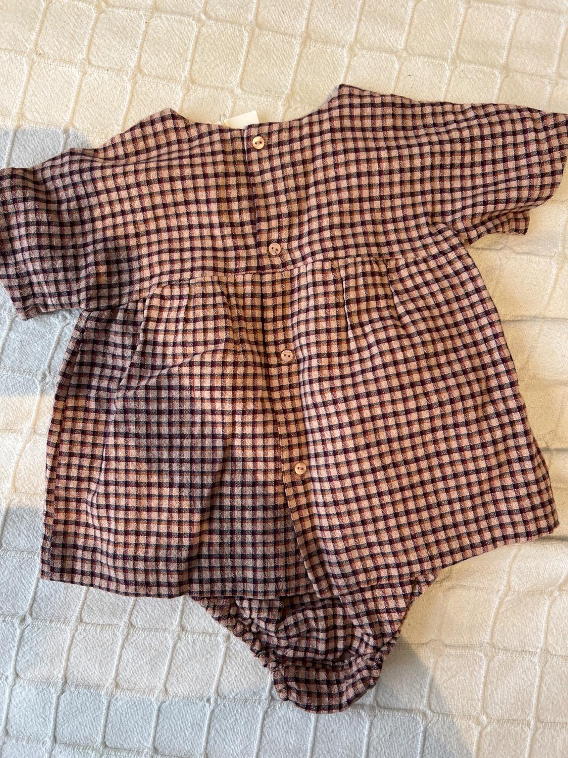 Children's brown and pink checked romper suit with buttons at the back, on a white padded surface.