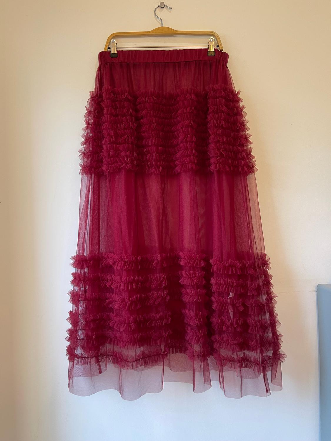Long red tulle skirt with ruffles, hanging on a wooden hanger against a white background.