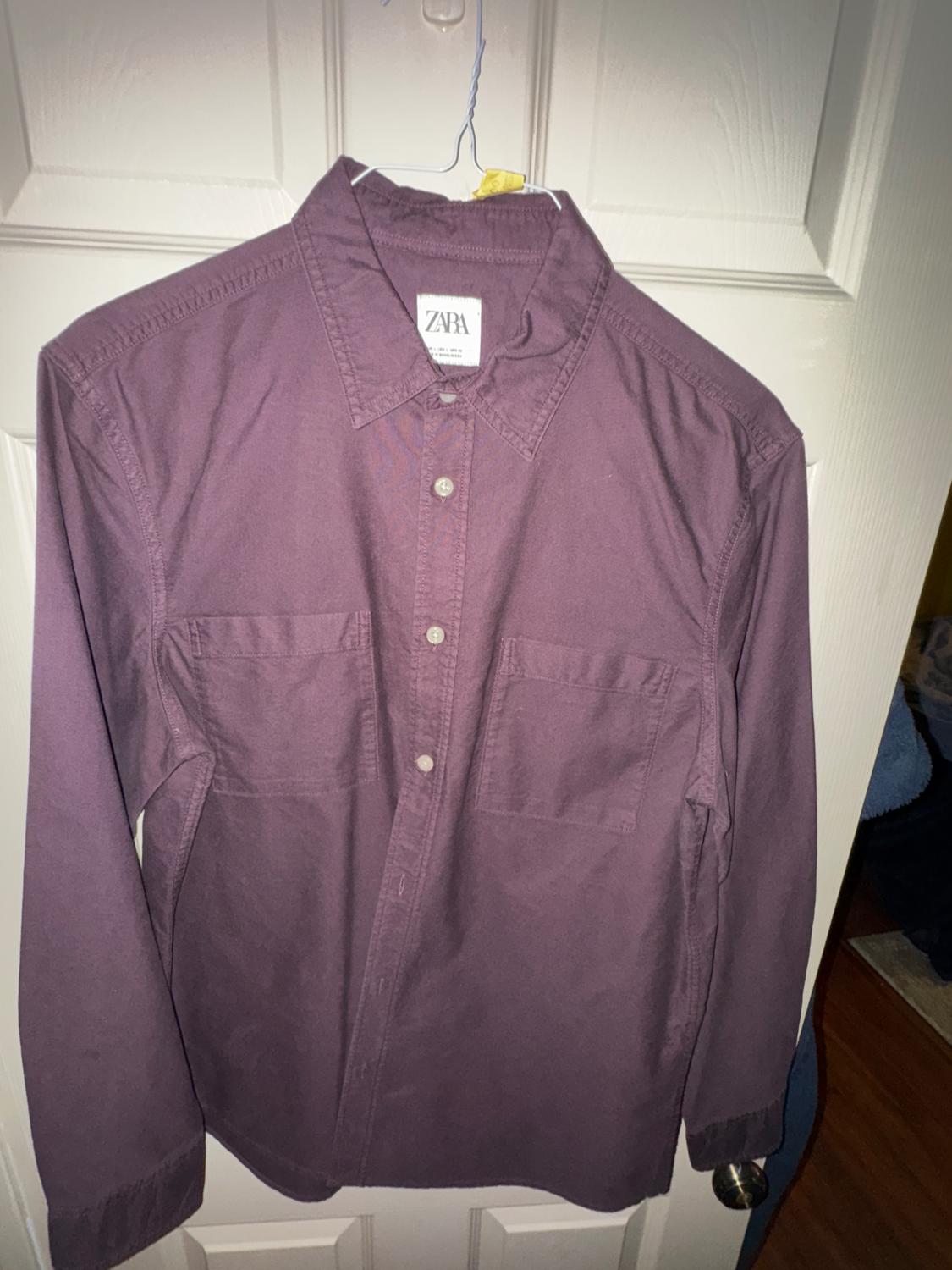 Purple long-sleeved shirt hanging on a hanger in front of a white door. Visible tag with the text "ZARA".