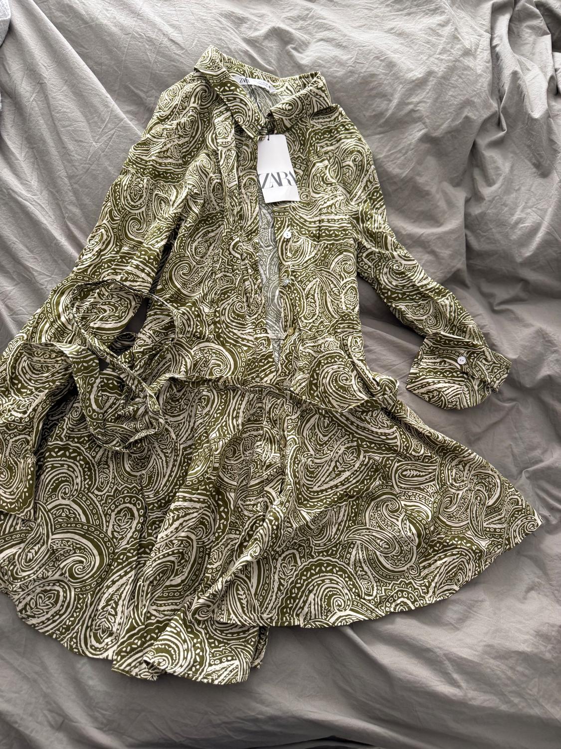 Green dress with white paisley print on a gray bed. Visible label with the text "ZARA".