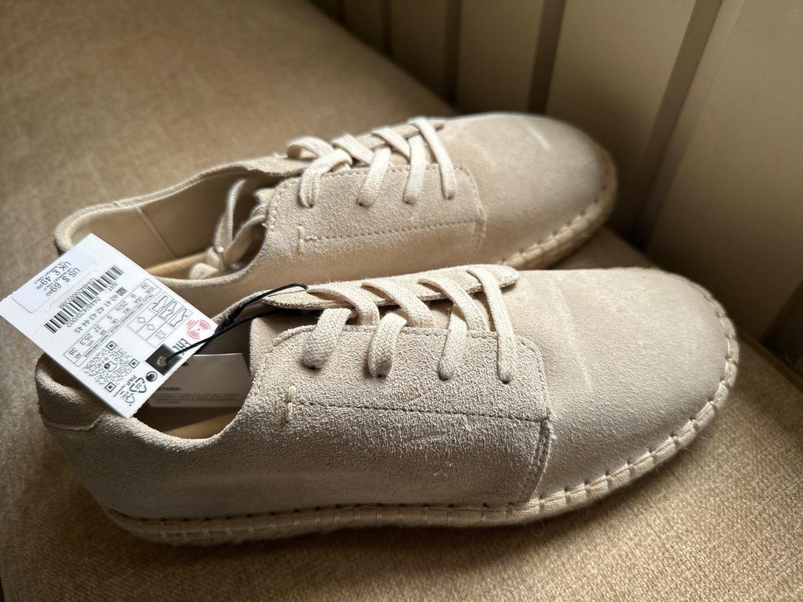 Beige suede lace-up shoes with braided soles on a fabric surface. Tag: US $ 69.90 UK £ 49.99.