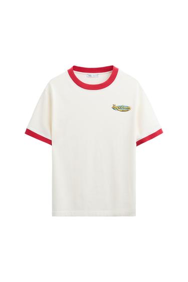 White T-shirt with red collar and sleeves. "Freedom" text on chest. Casual and relaxed style. White background.