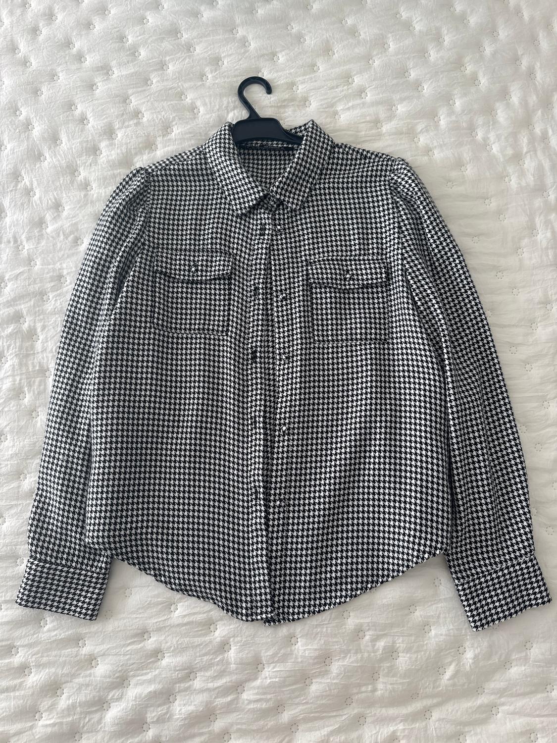 Black and white checked shirt with front pockets, hanging on a hanger over a textured white bedspread.