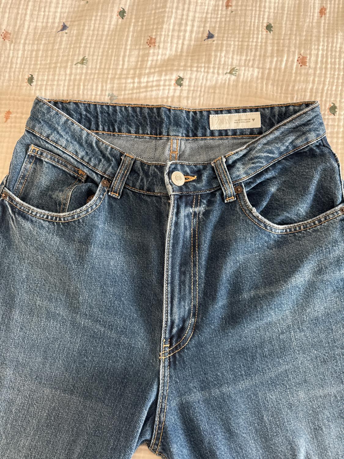 Blue jeans on a white quilt with small coloured patterns. The button and seams are visible. Internal label present.