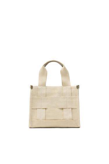 Beige fabric handbag with interlocked design and short handles, on a white background.