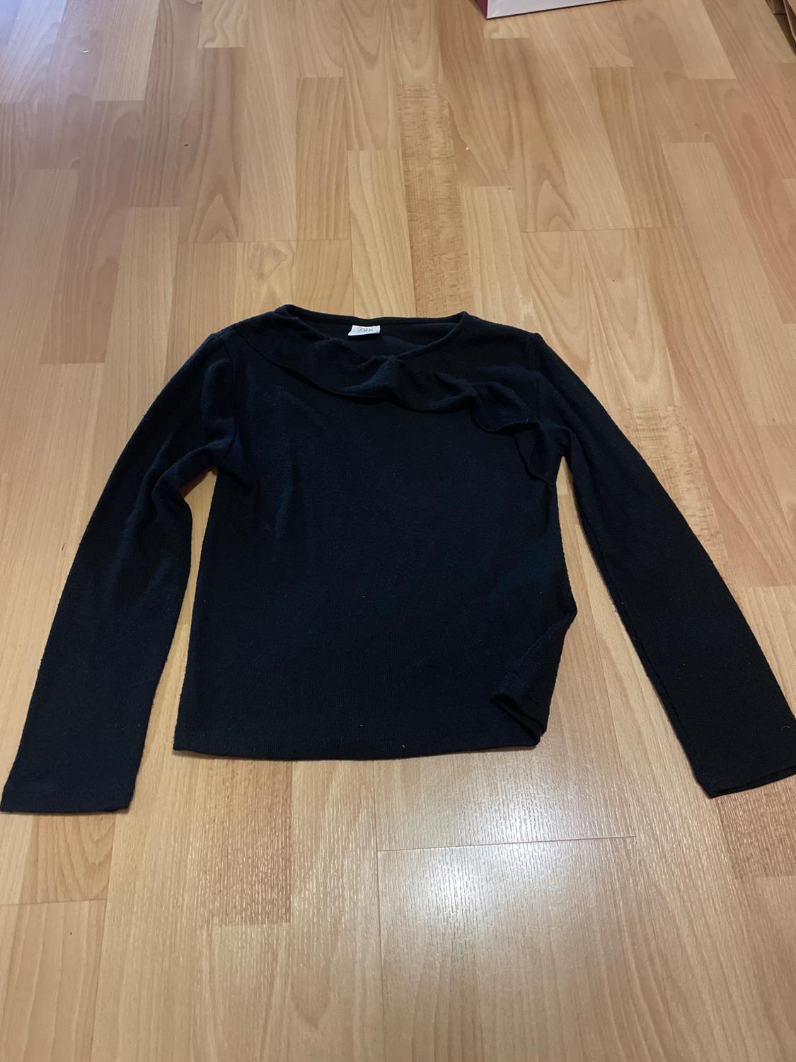 Black long-sleeved jumper on a light wood floor. Simple, fitted design, ideal for a casual look.