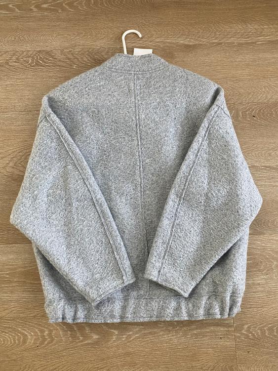 Textured gray wool jacket, seen from behind, hanging on a hanger over a light wood floor.