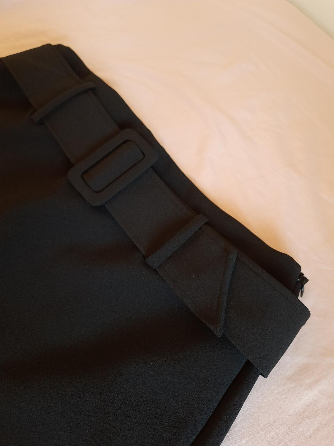 Detail of black belt with rectangular buckle on garment.