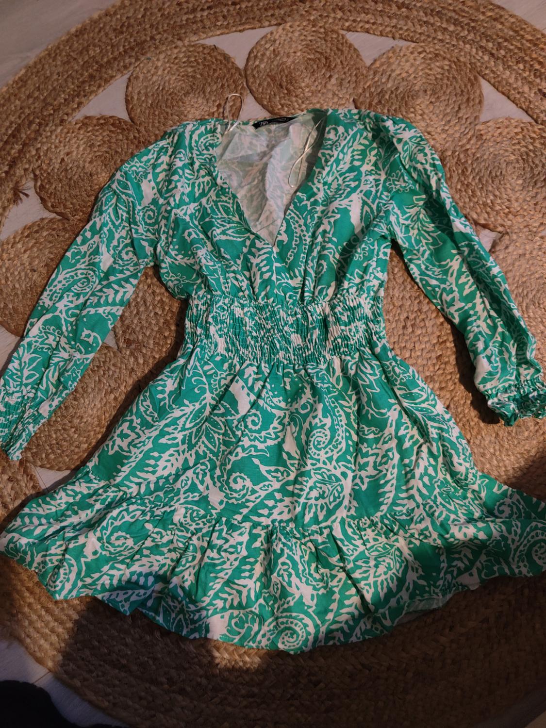 Green dress with white leaf print, long sleeves and ruched waist, over a spiral-braided jute rug.