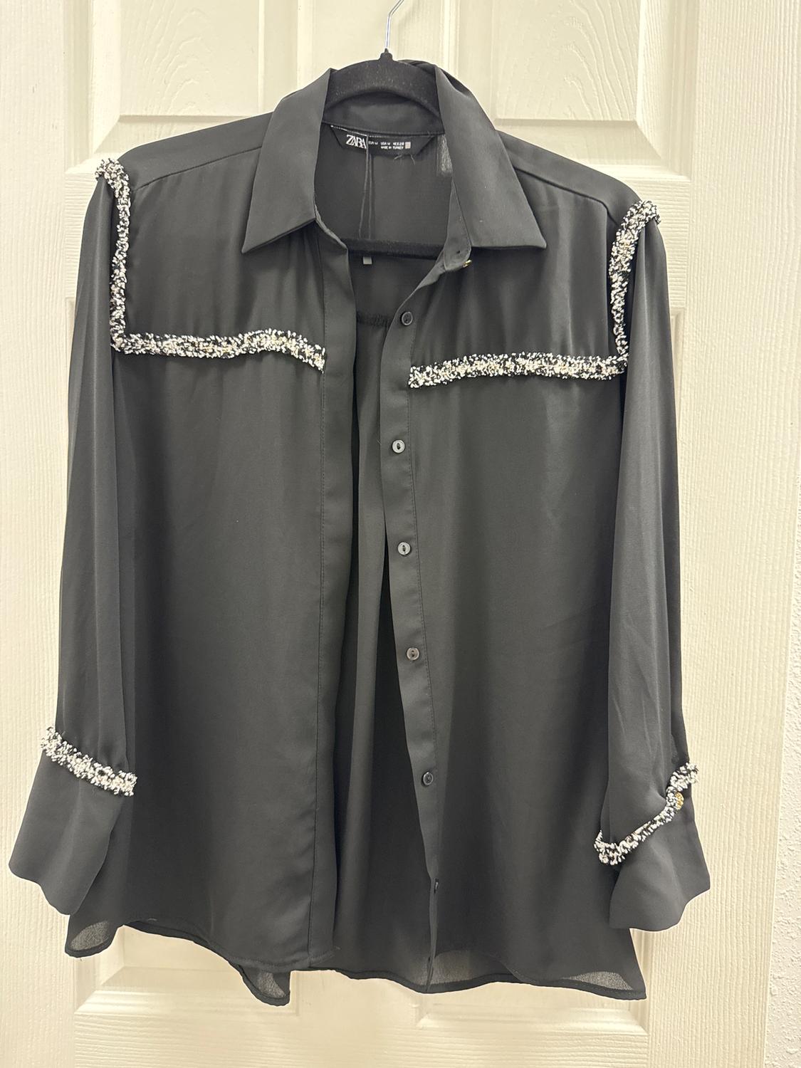 Black shirt hanging on a door, with diamante details on the shoulders, chest, and cuffs. Elegant and modern style.