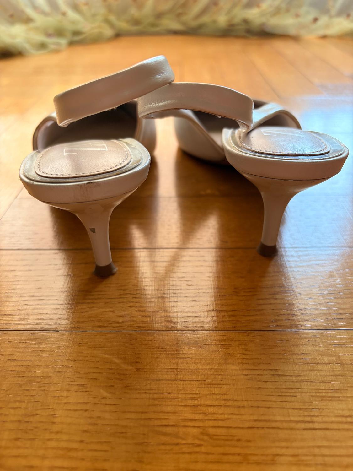 Μπεζ slingback γυναικεία παπούτσια με χαμηλό τακούνι και καφέ λεπτομέρειες, όπως φαίνονται από πίσω σε ξύλινο δάπεδο.