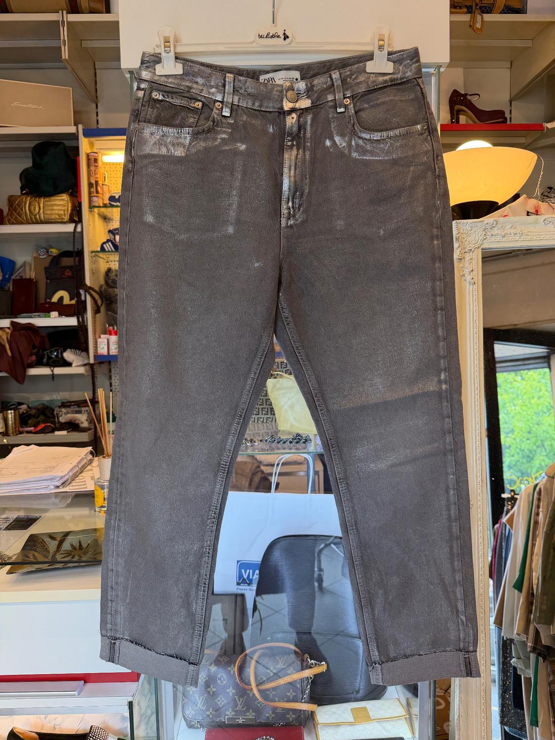 Metallic grey trousers hanging in a shop, surrounded by handbags and boxes. Boutique atmosphere with warm lighting.