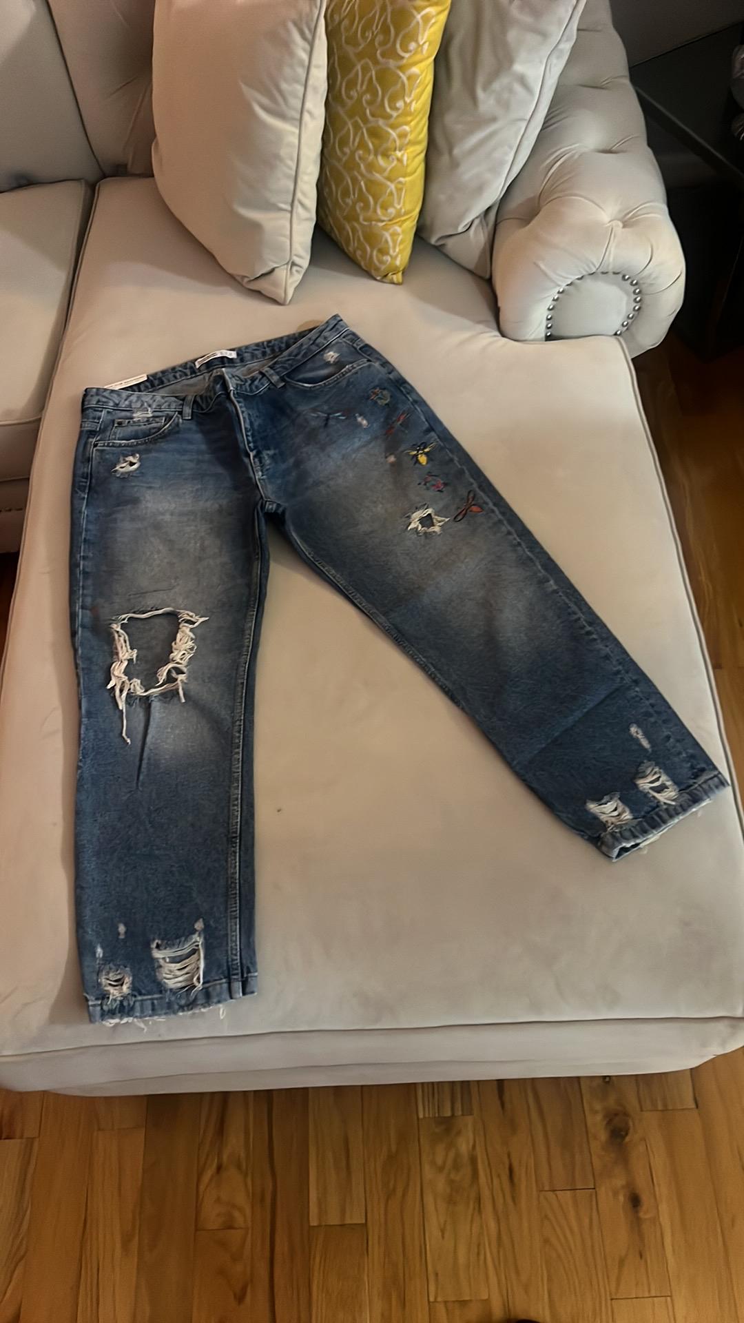 Front view of blue jeans with ripped legs and coloured prints.