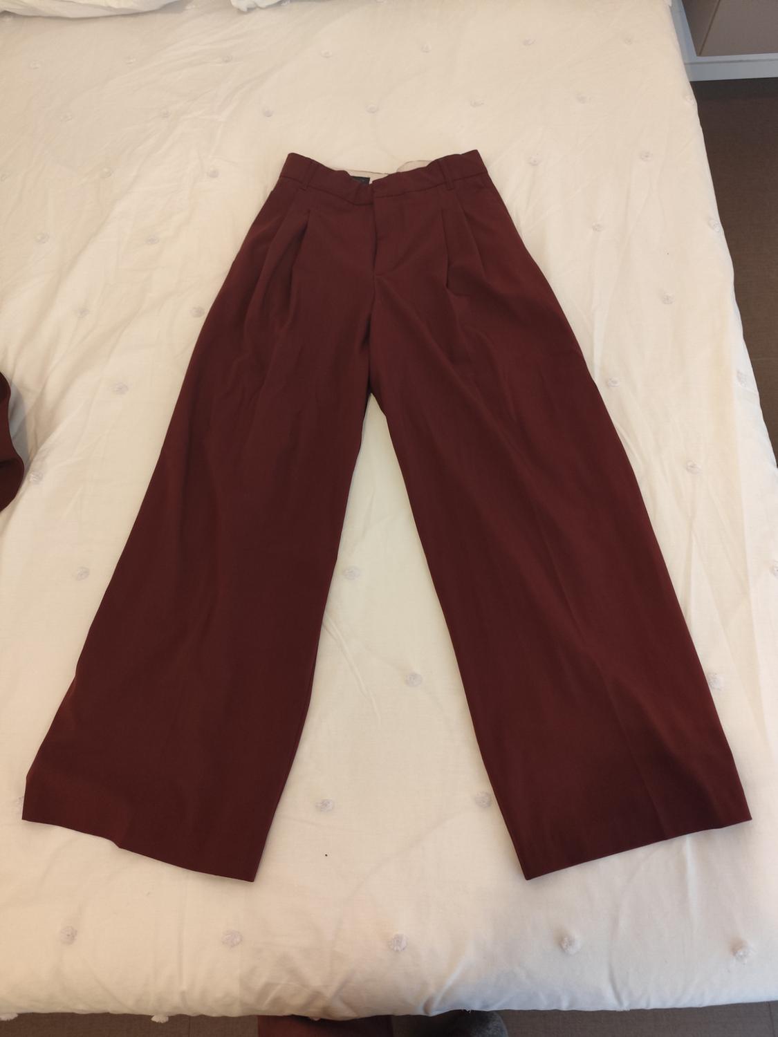 Burgundy wide-leg trousers placed on a white bed with button details.