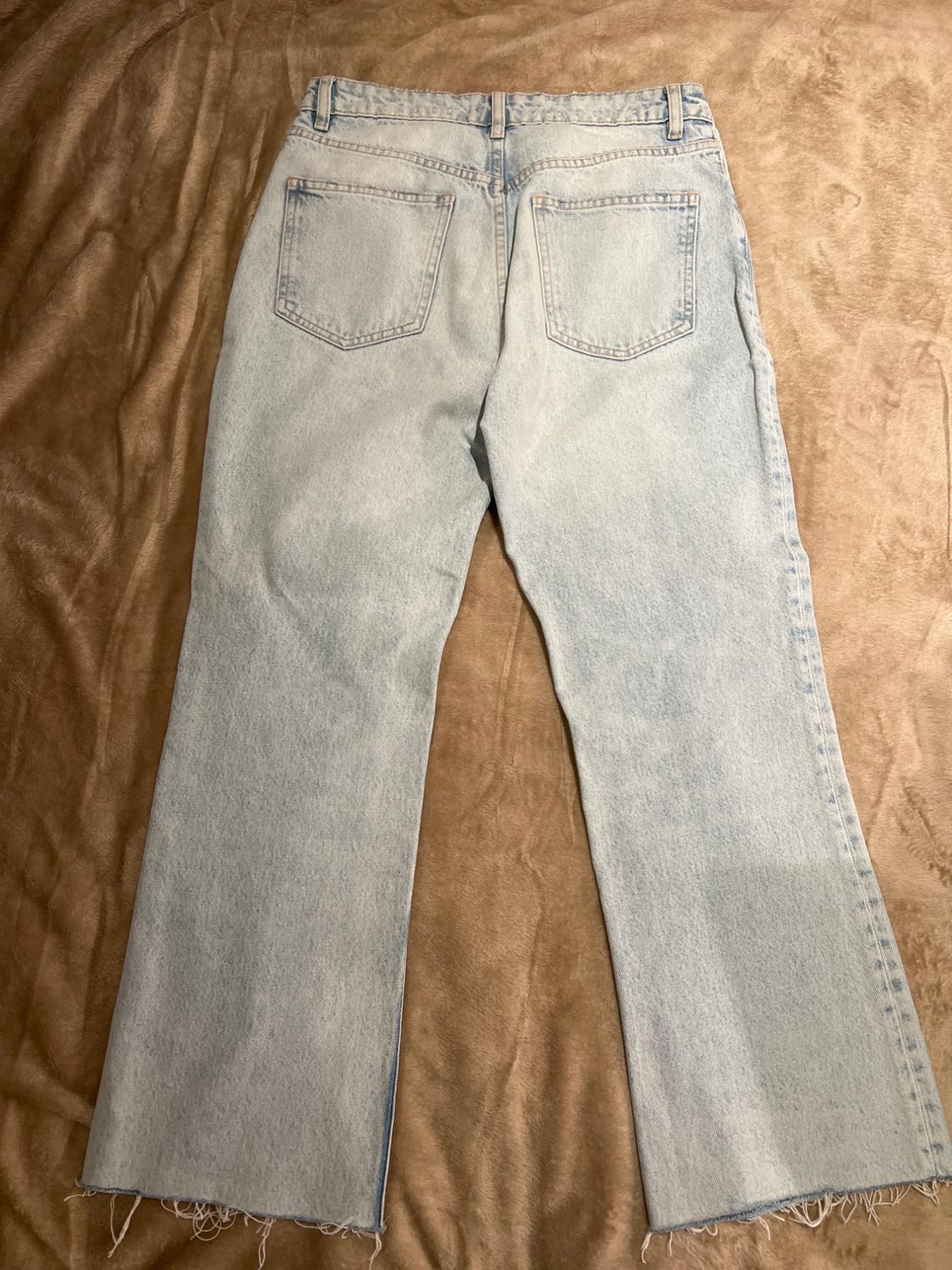 Light blue denim jeans with back pockets, placed on a brown surface.
