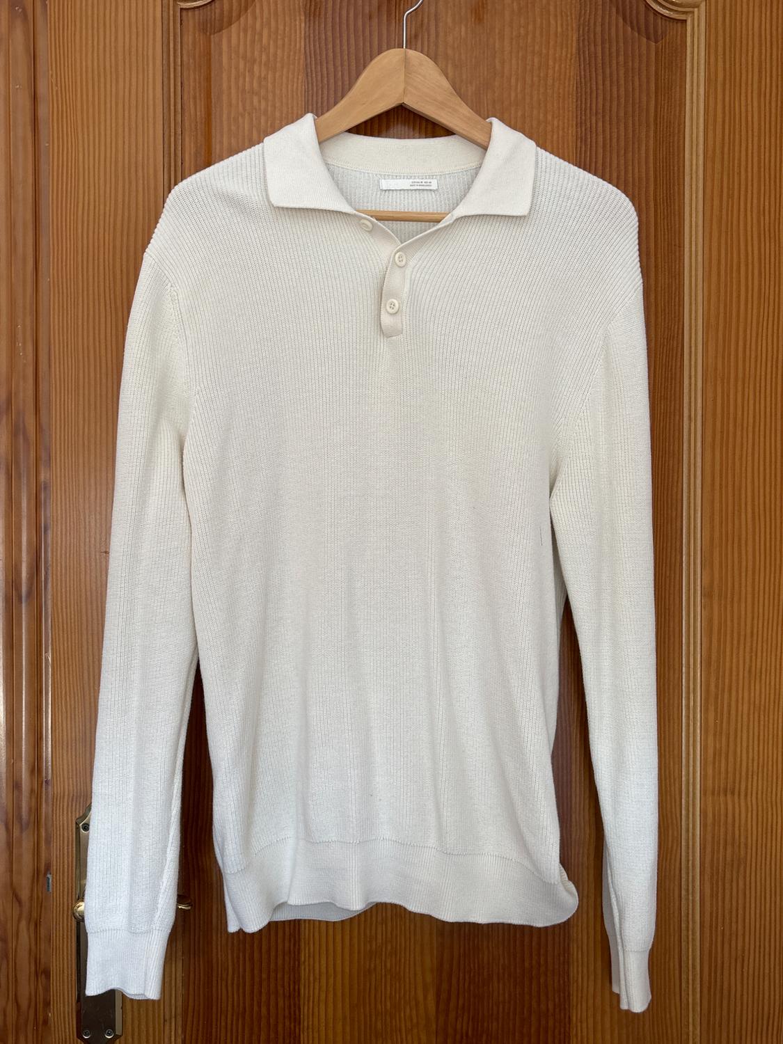 Fine knit white jumper with a collar and buttons, hanging on a wooden hanger over a brown wooden door.