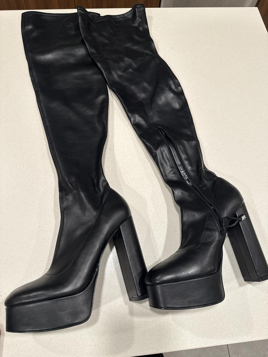 Black high-heeled platform boots with a chunky heel on a light surface. One boot has a visible side fastening.