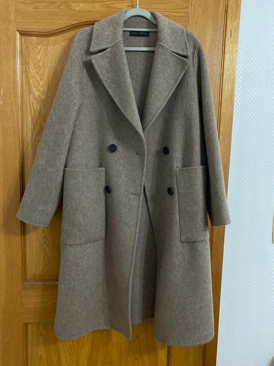 Long light brown double-breasted coat with buttons and pockets, hanging on a wooden door.