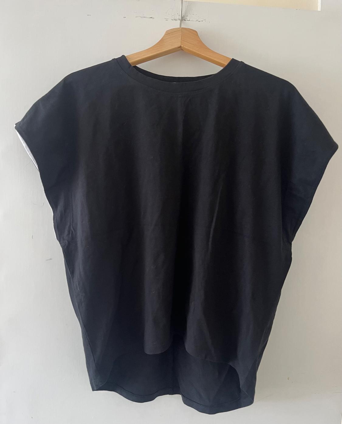 Loose black t-shirt hanging on a wooden hanger against a white wall. Casual and minimalist design with an asymmetric hem.