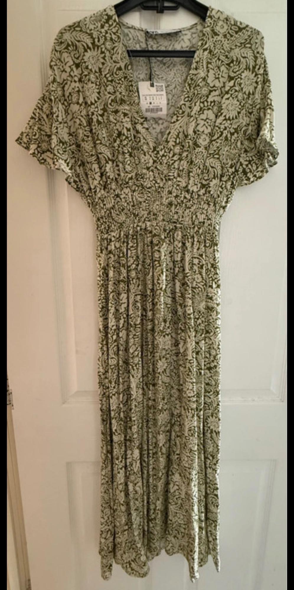 Long green and white floral print dress with short sleeves and a V-neck, hanging on a hanger over a white door.