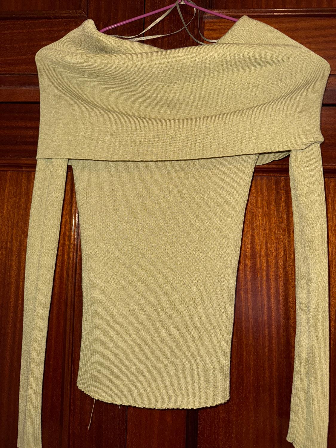 Beige knitted boat neck jumper, hanging on a pink hanger over a wooden door.