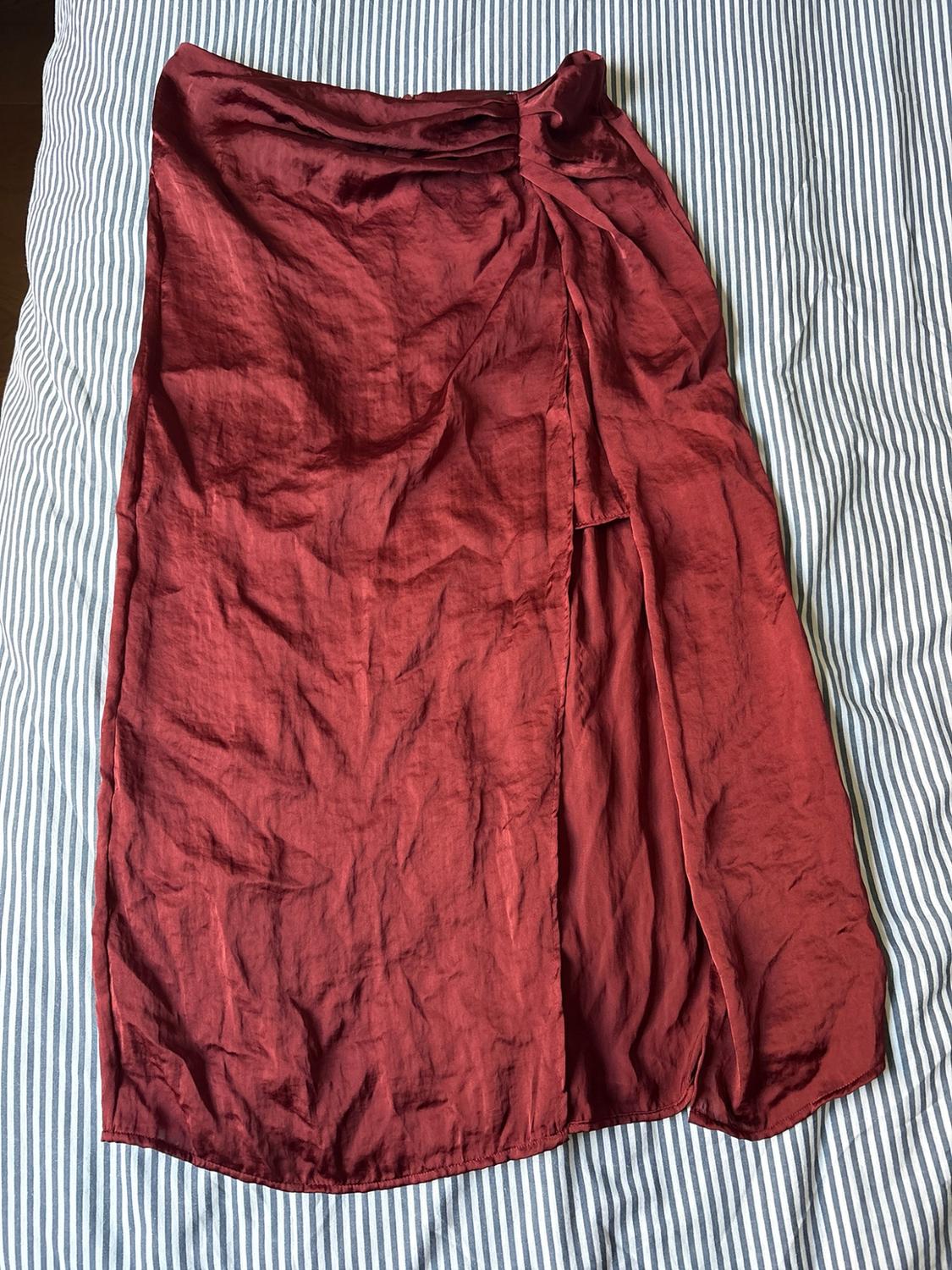 Maroon satin midi skirt with a side split, creased and laid out on blue and white striped sheets.
