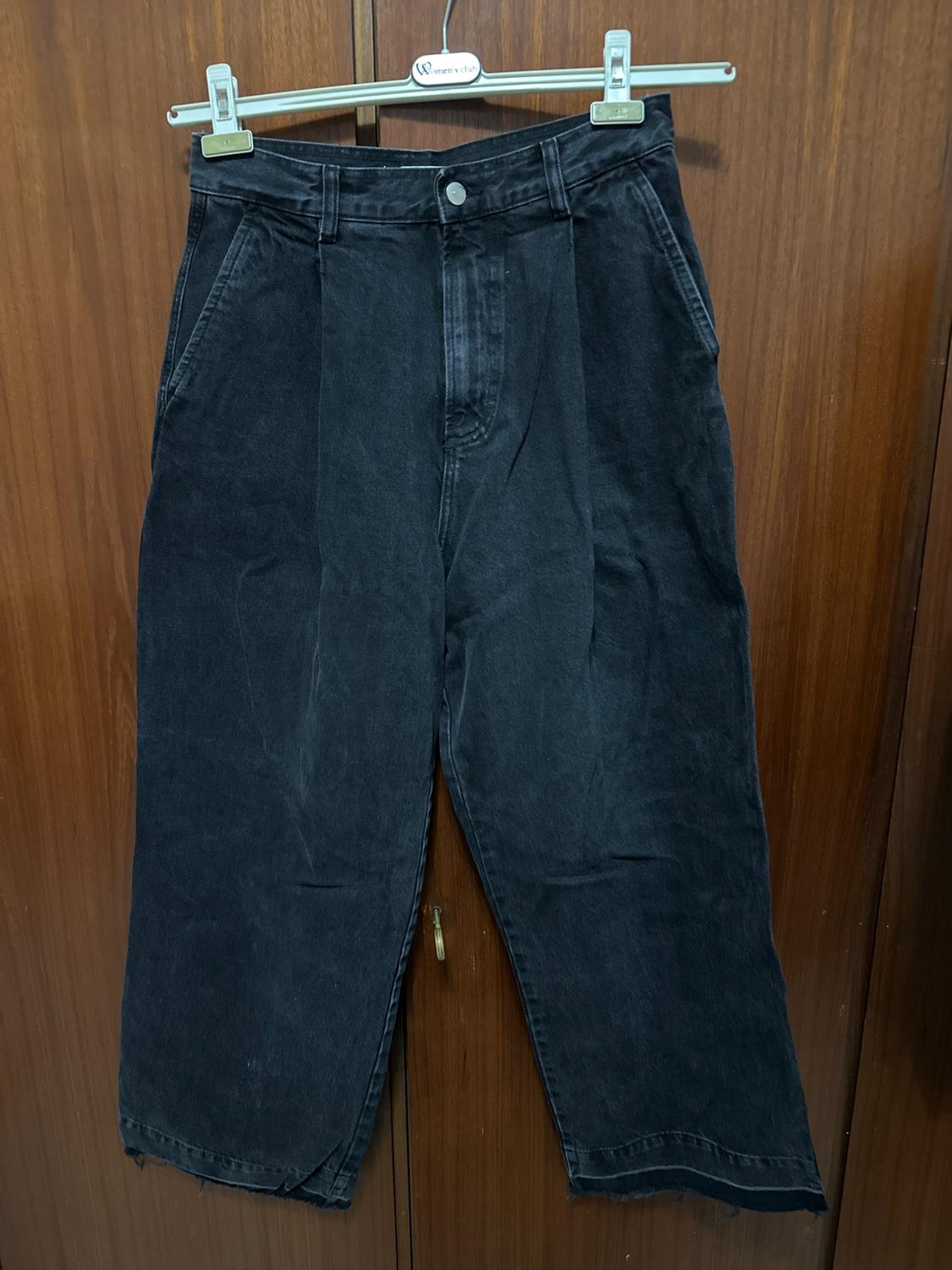 Black denim trousers hanging on a metal hanger in front of a wooden door.