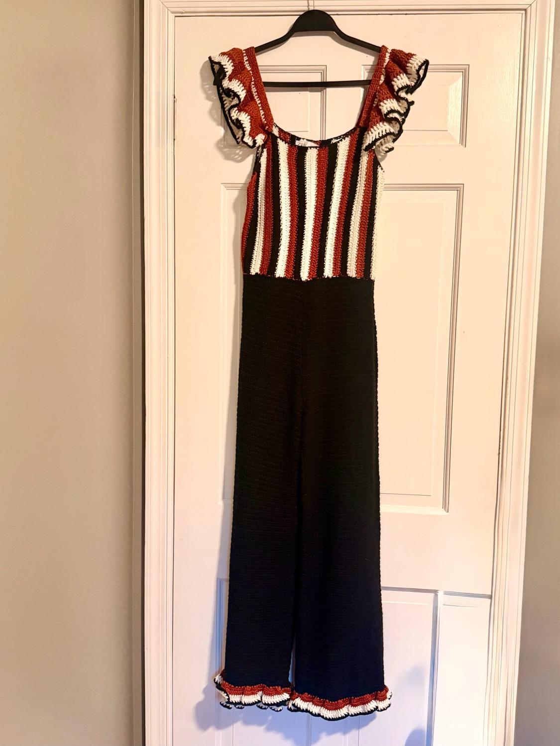 Polka-dot jumpsuit hanging on a white door. Black, white and burgundy striped top with ruffles. Black trousers with a ruffled hem.