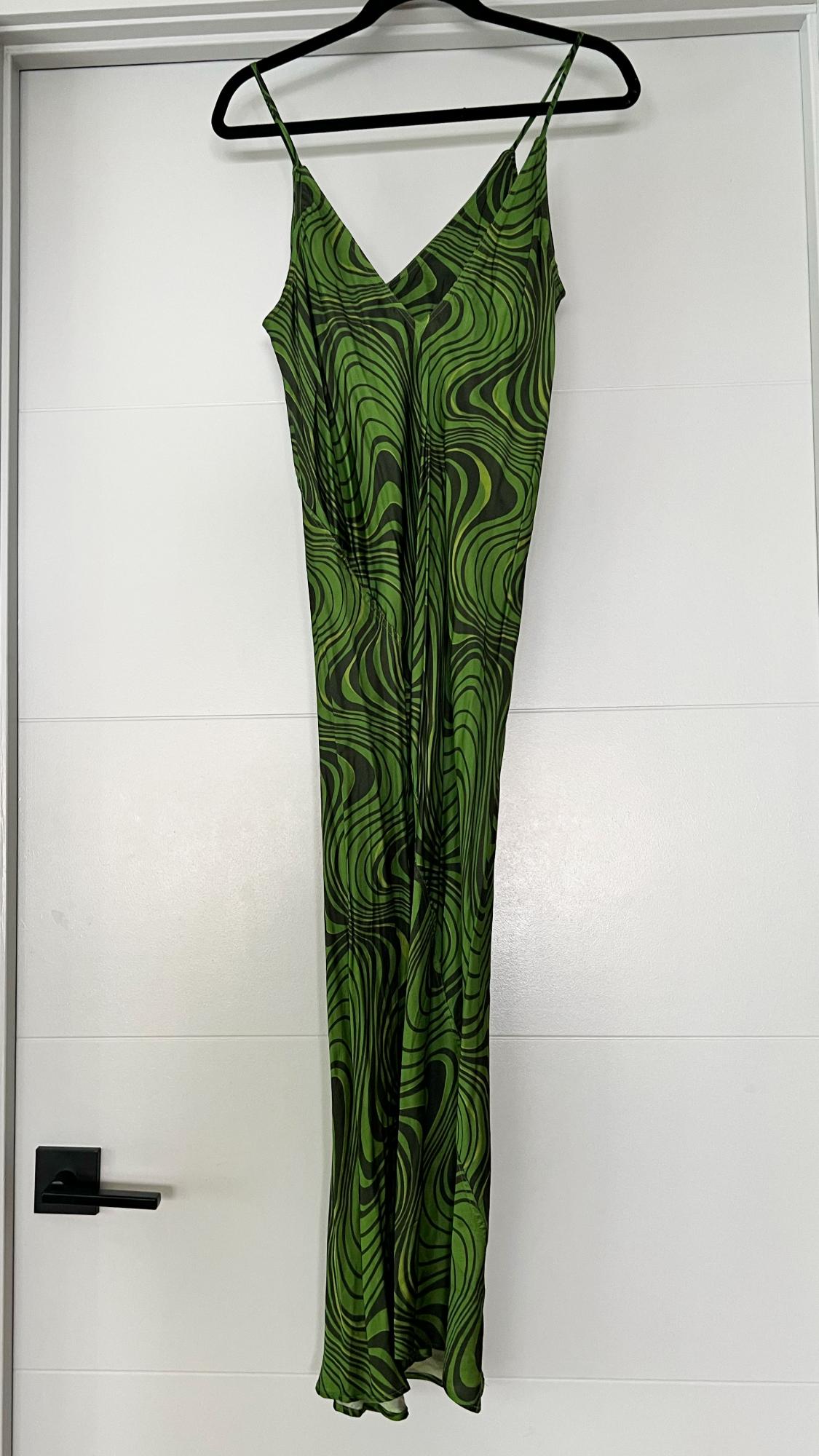 Long spaghetti strap dress with a psychedelic print in shades of green and black, hanging on a hanger in front of a white door.