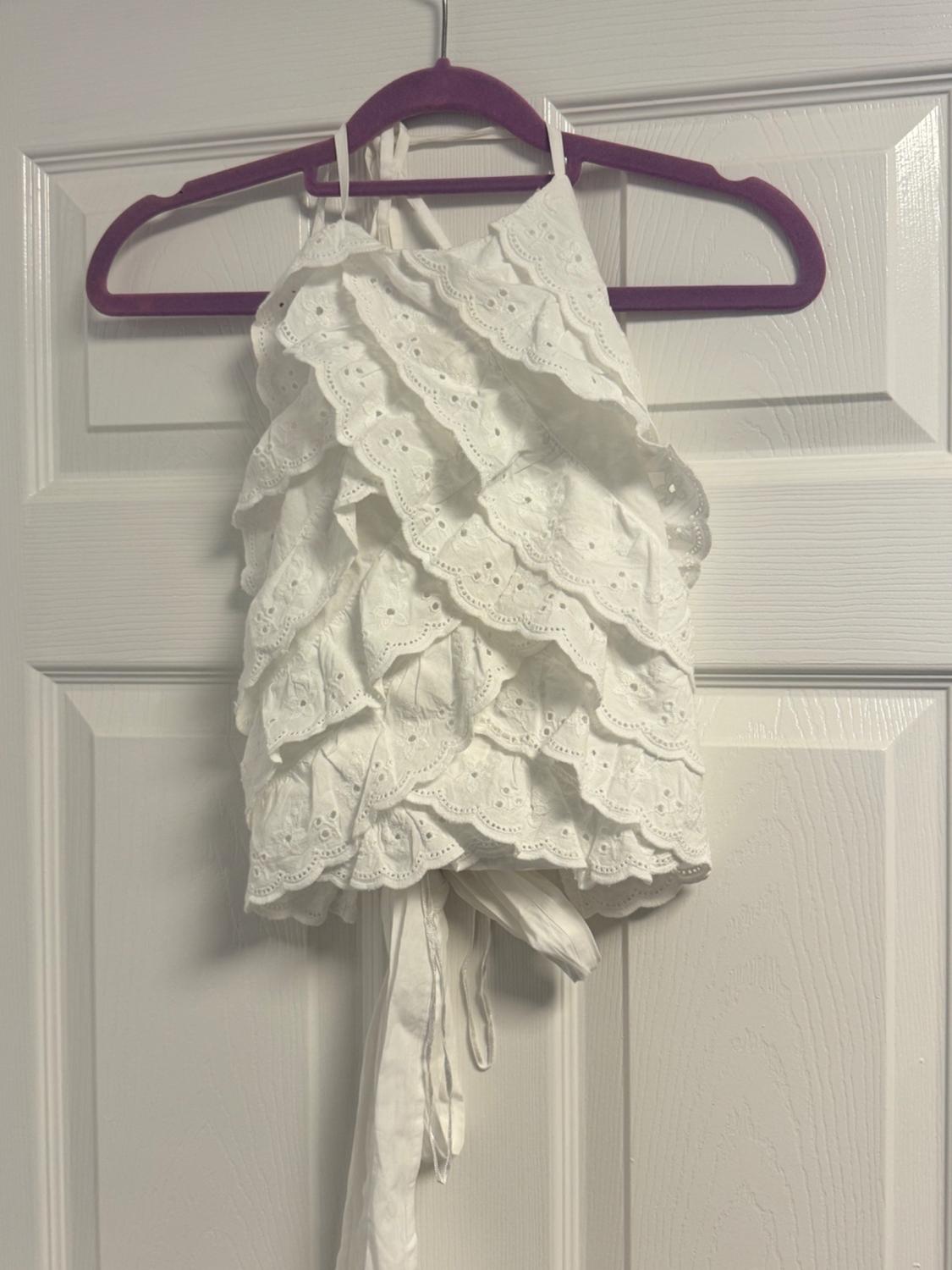 White top with frills and embroidery, hanging on a purple hanger on a white door.