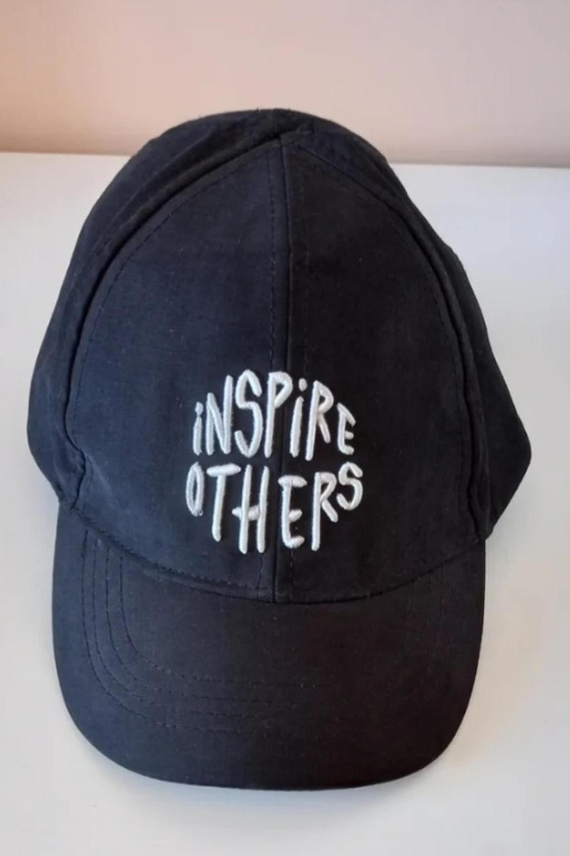 Detail of black cap with embroidered text 'INSPIRE OTHERS'.