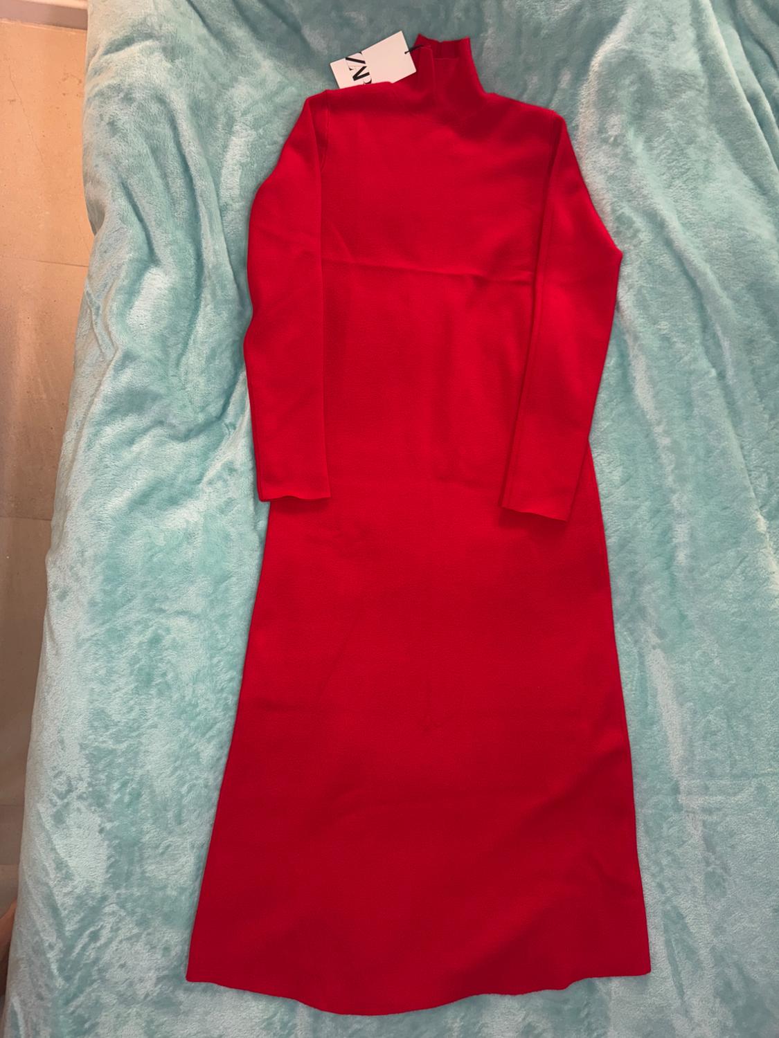 Red long-sleeved, high-necked dress on a light blue blanket. Label visible on the collar.