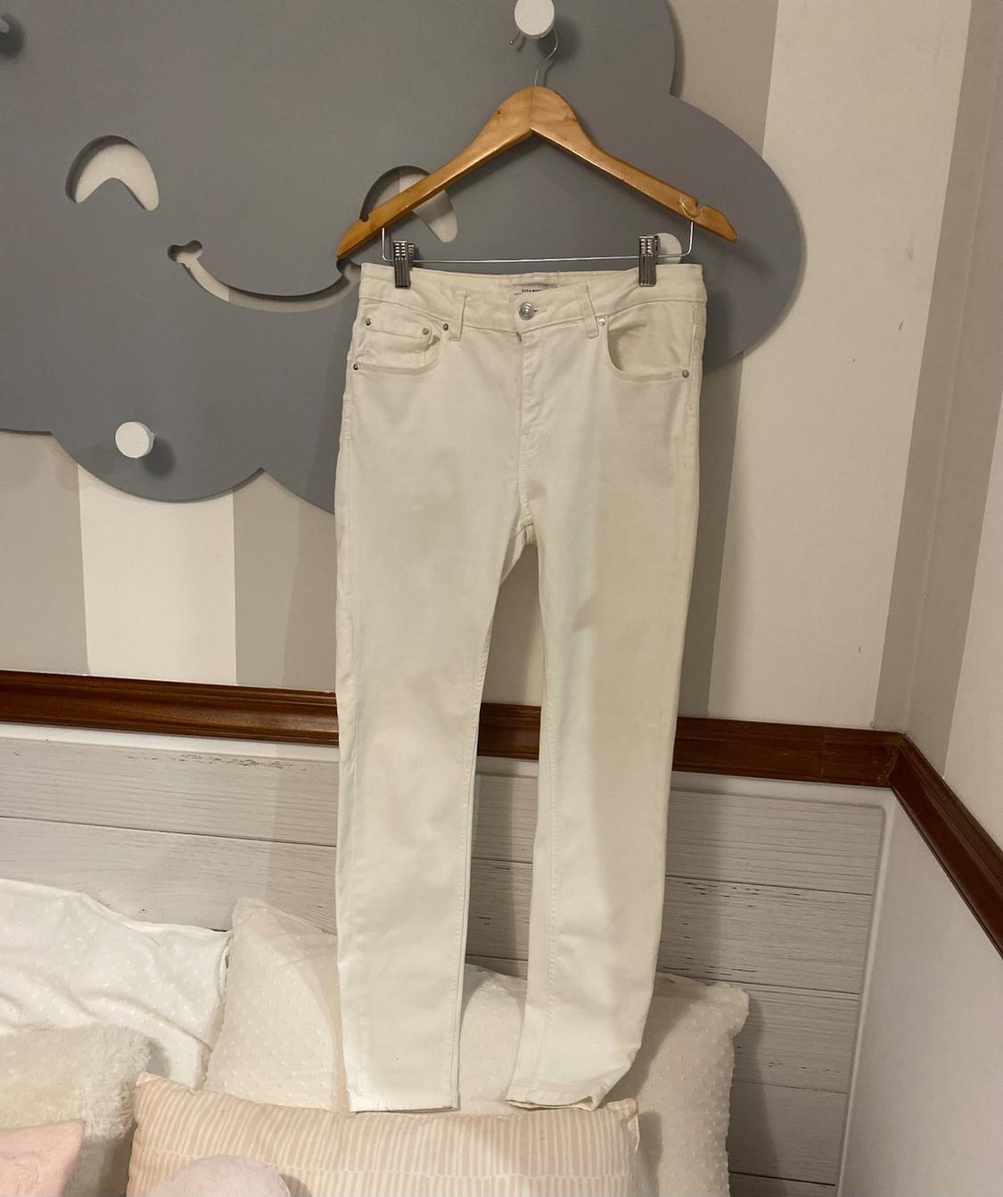 White trousers hanging on a wooden hanger against a grey cloud-patterned wall. Background with white and beige cushions.