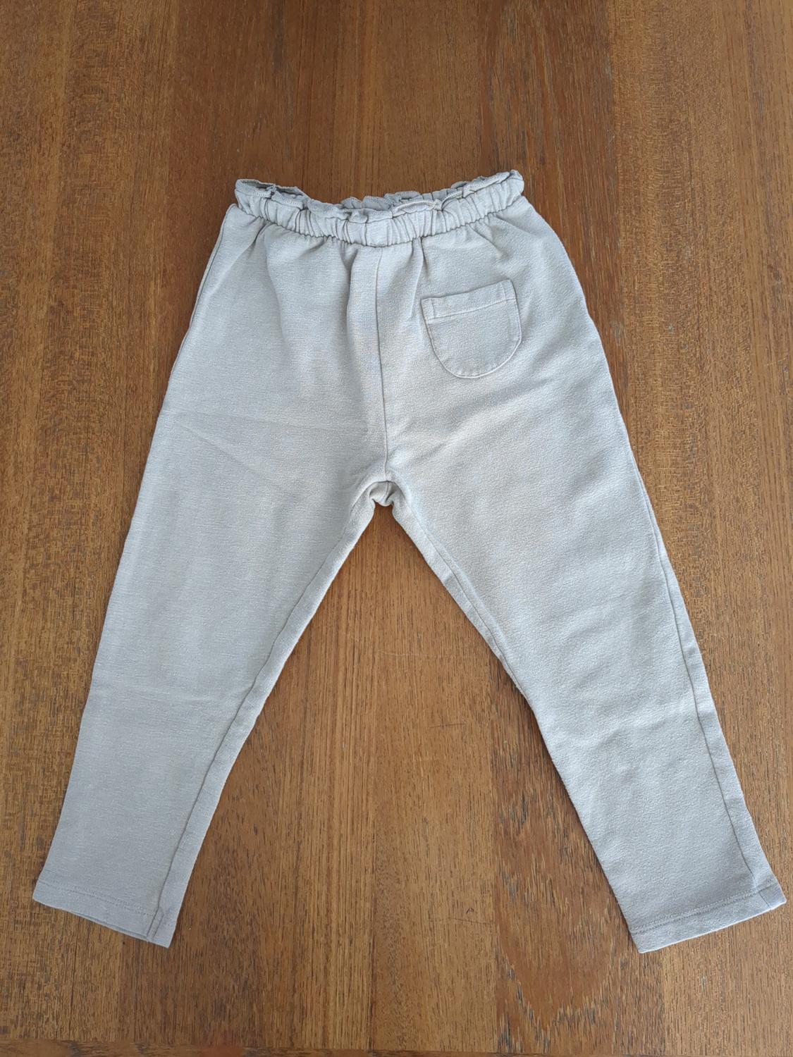 Beige children's pants with an elastic waistband and back pocket, on a brown wooden surface.
