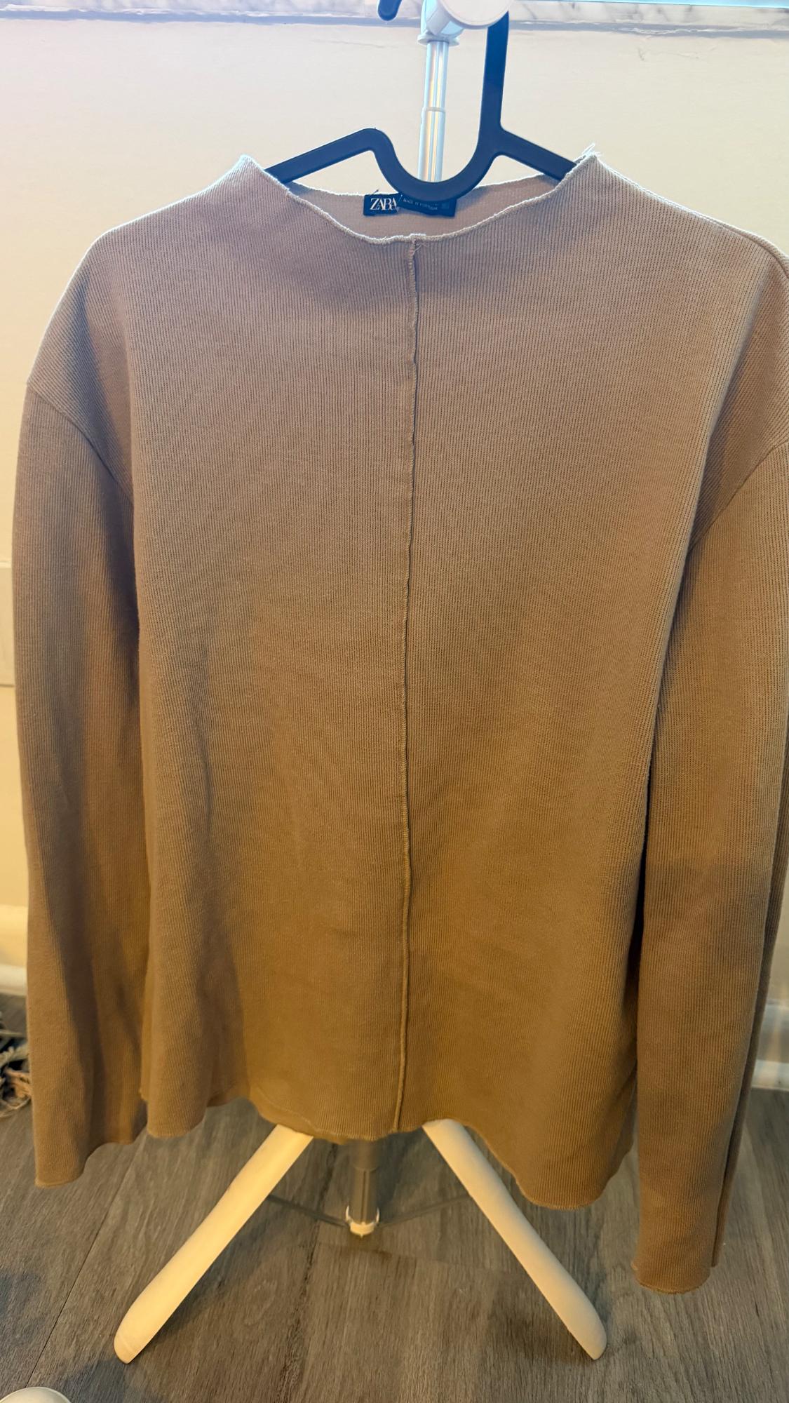Beige ribbed long-sleeve sweater with a center seam, hanging on a black hanger against a white background. Label with the text ZARA.