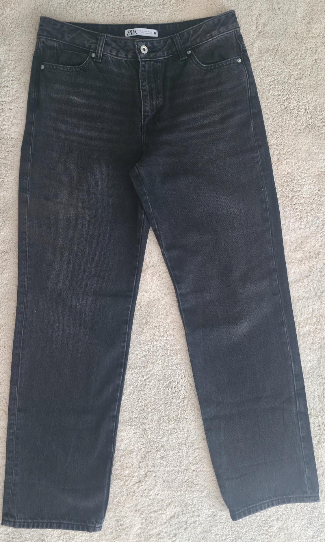 Black denim pants with a straight cut and washed finish, photographed on a light-colored rug. Interior label with the text ZARA.