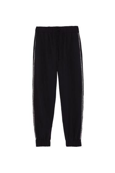 Black joggers with an elasticated waistband, adjustable drawstring, elasticated cuffs and a shiny side stripe, on a white background.