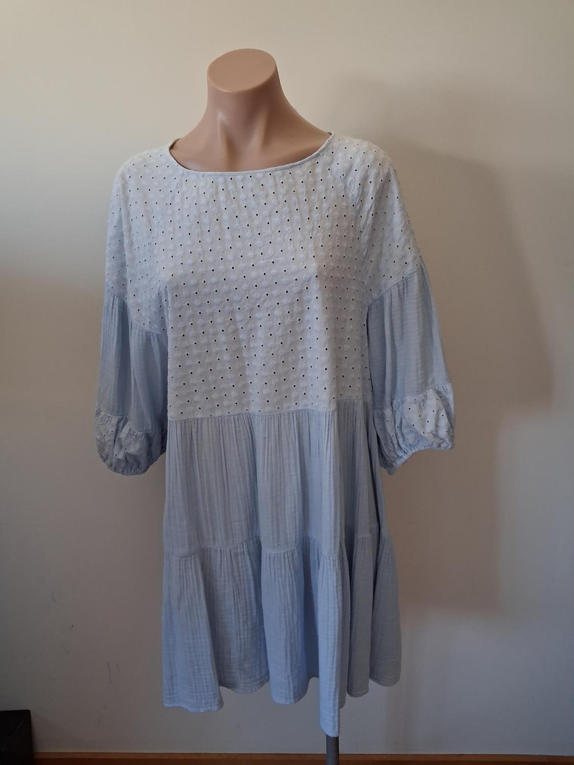 Mannequin wearing a light blue, long-sleeved, loose-fitting dress, with small polka dot details on the upper part.