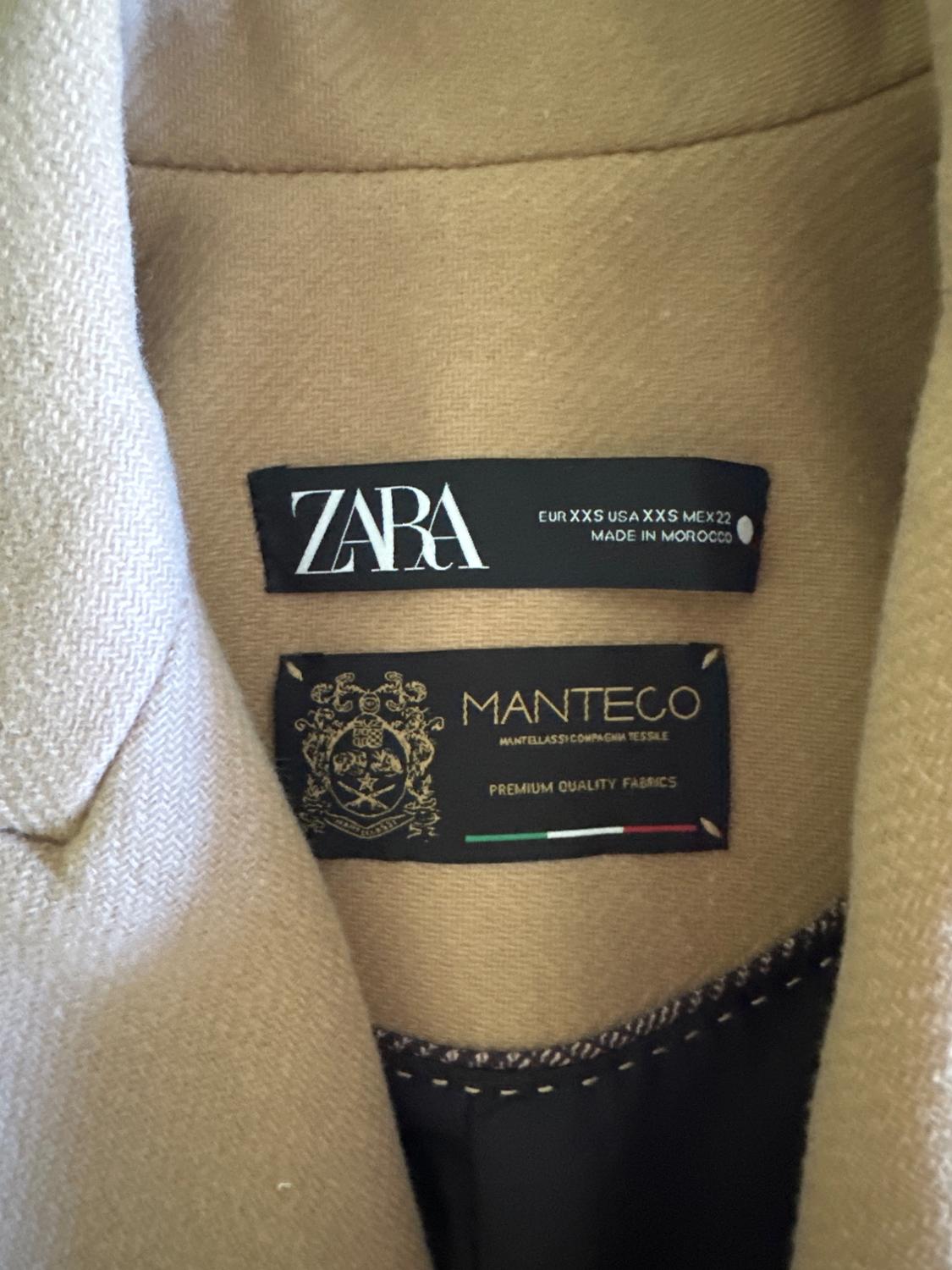 Beige coat tag with text: "ZARA EUR XXS USA XXS MEX 22 MADE IN MOROCCO" and "MANTECO PREMIUM QUALITY FABRICS".
